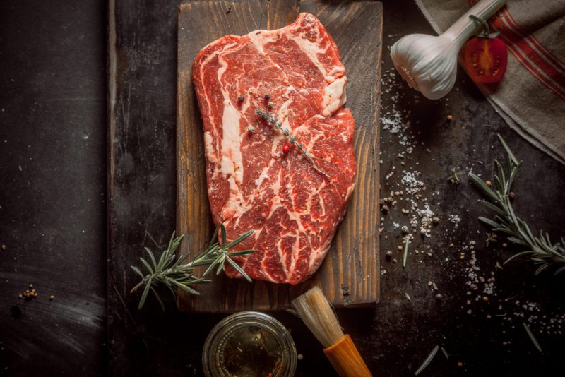 Close up Wooden Chopping Board with Raw Beef Meat on a Rustic Table with Herbs and Spices