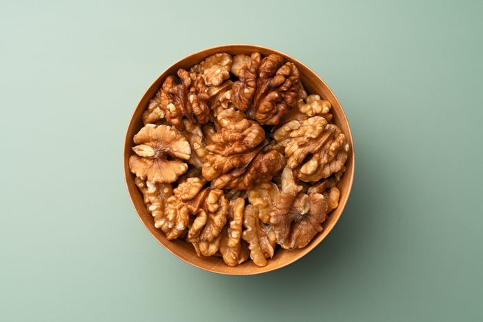 Shelled Walnuts in Wooden Bowl on Green Background