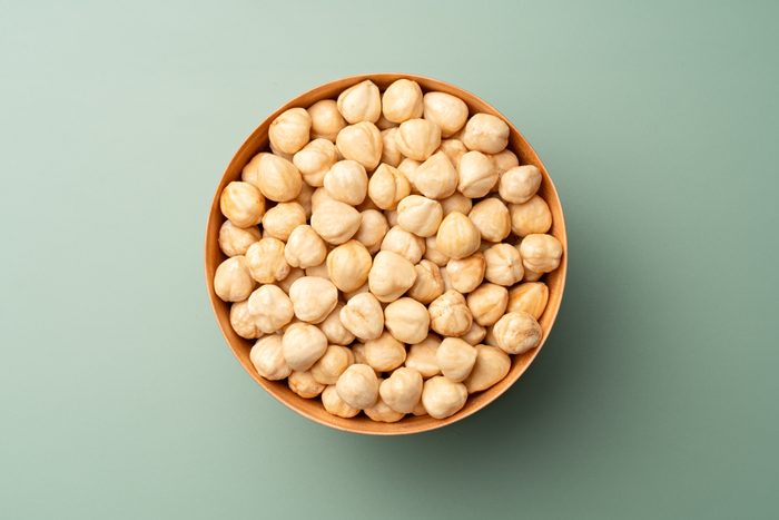 Shelled Hazelnuts in Wooden Bowl on Green Background