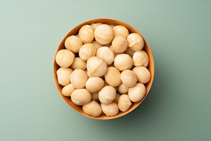 Macadamia Nuts in Wooden Bowl on Green Background