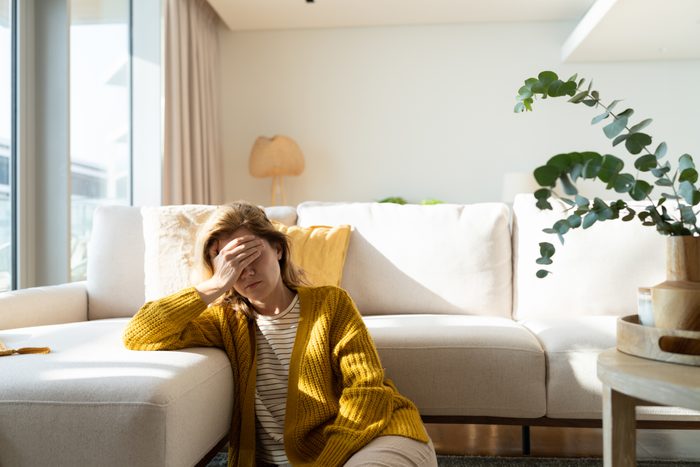 Woman having headache and holding her head while sitting on the floor at home