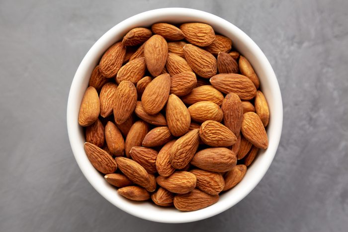 Raw brown almonds in a bowl on a gray surface, top view. Flat lay, overhead, from above.